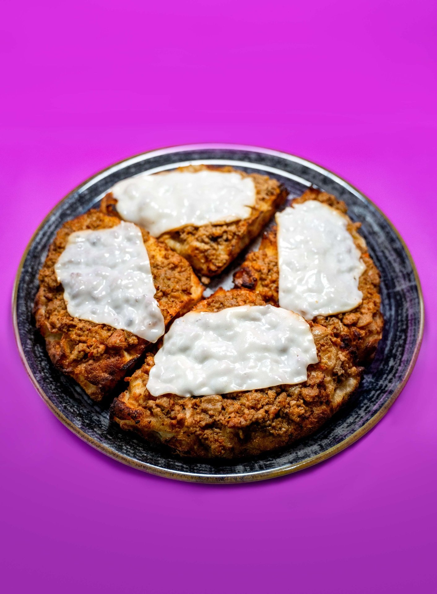 Pizza tonda al ragù con stracciatella su piatto scuro
